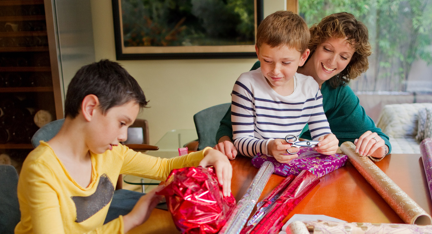 lady helping two boys wrap presents
